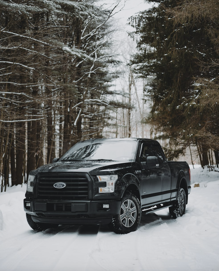 A black ford truck parked in a snowy forest.
