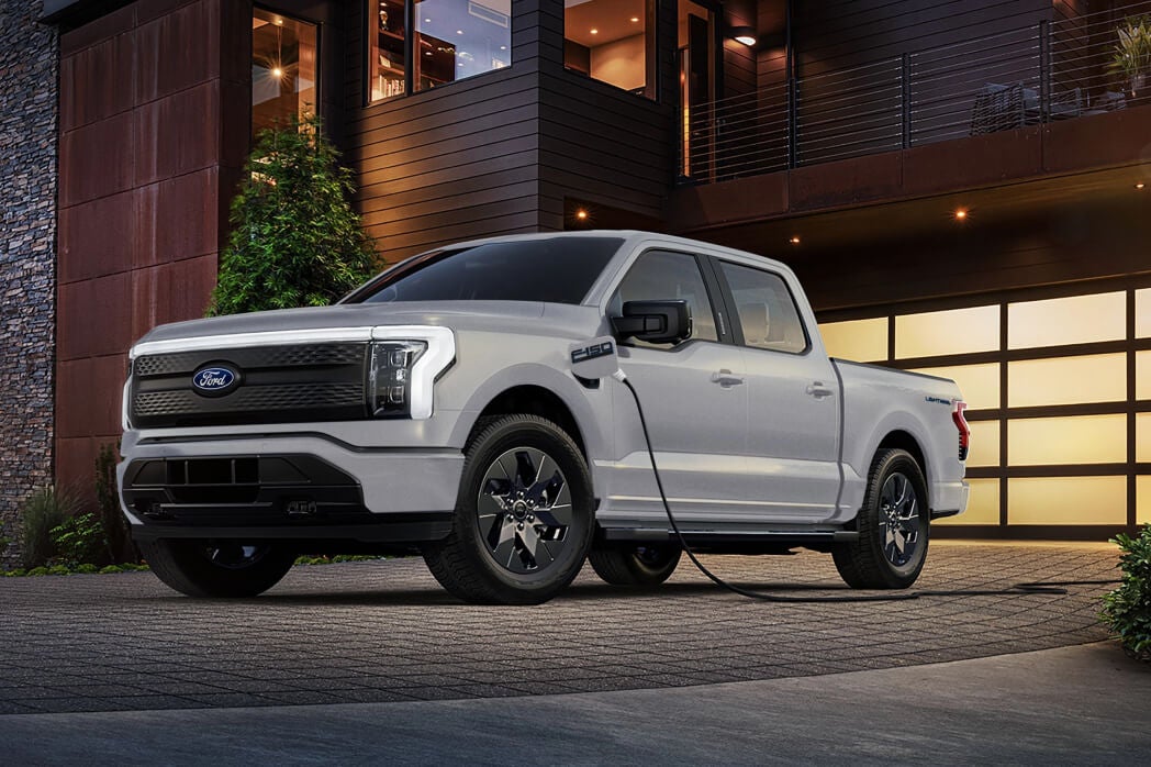 2025 Ford F-150 Lightning Electric Truck charging in modern driveway at sunset